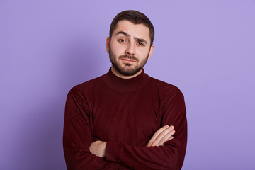 Obraz premium Indoor portrait of surprised impressed handsome man having folded arms, raising one eyebrow, having bewildered facial expression, looking directly at camera, being emotional. People concept.