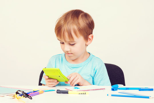 Smart little boy holding calculator. Child doing homework. Back to school concept. School supplies on a white desck.