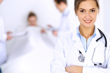 Female doctor smiling on the background with patient in the bed and two doctors