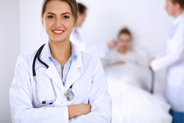 Fototapeta premium Female doctor smiling on the background with patient in the bed and two doctors