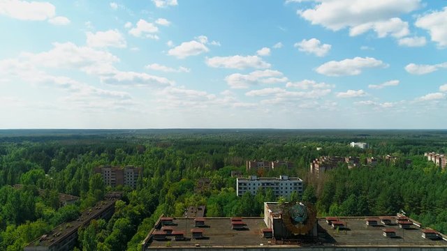Aerial view of abandoned buildings and streets overgrown with trees in city Pripyat near Chernobyl nuclear power plant. Exclusion Zone. Camera moving away. Sign of USSR on the roof. 4K drone footage.