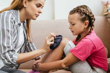 mother holding ice bag compress on painful knee of upset daughter
