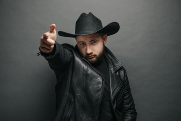 Cowboy studio portrait of a man wearing learher jacket and a hat with serious face