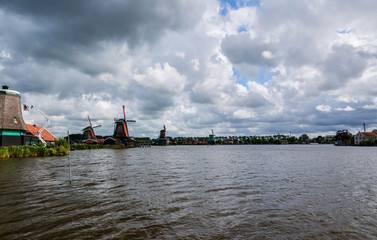 Zaanse Schans, Holland, August 2019. Northeast Amsterdam is a small community located on the Zaan River. View of the mills on the river bank, they stand out with their bright colors. Cloudy day.