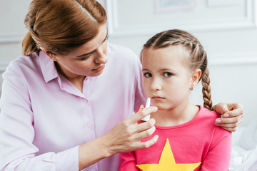 mother giving nasal spray to ill daughter with runny nose