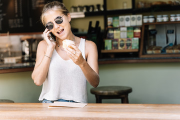 Blonde girl with sunglasses talking on her mobile phone with a cinnamon roll in the hand