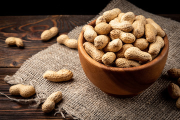 Peanut in the shell in wooden bowl on dark wooden background.