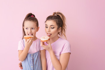 Funny young woman and little girl with donuts on color background