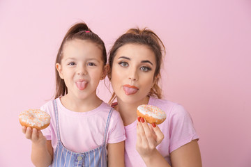 Funny young woman and little girl with donuts on color background