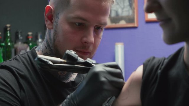 Shooting of young tattooer getting tattoo of snake in salon