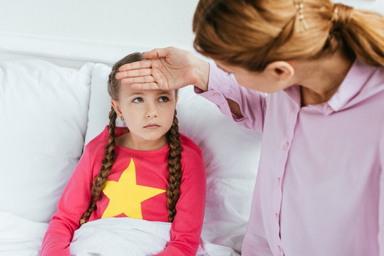 worried mother touching forehead of ill daughter with fever