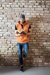 Fototapeta na wymiar Young man in cap standing at wall reading book