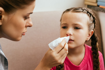 worried mother holding napkin near upset daughter with nasal bleeding