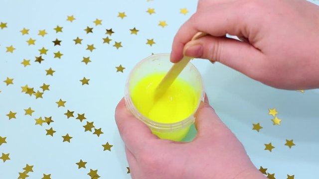 The girl makes yellow green slime. Making slime on a blue background with stars. The process of making a fashionable liquid toy.