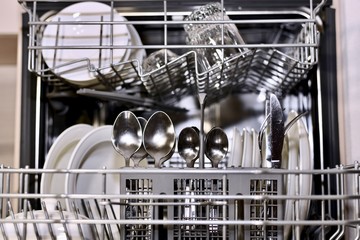 The dishes are clean in an open dishwasher large with a focus on cutlery.