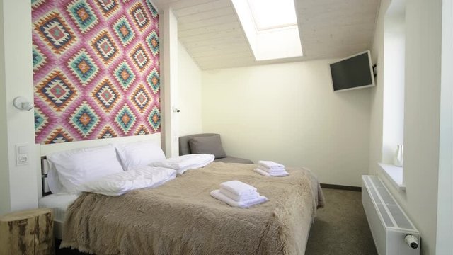 Interior of a spacious hotel bedroom on attic floor with fresh linen on a big double bed. Cozy contemporary mansard room in a modern house.