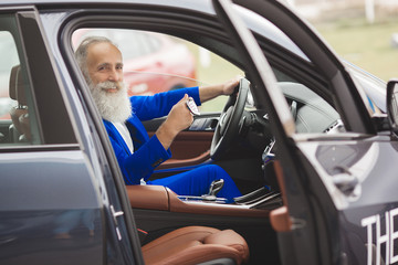 Naklejka premium Old handsome man inside the car. Bearded mature male in the automobile. Confident businessman buying the car.