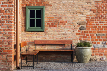 Fototapeta na wymiar Empty bench in brick wall corner with small window. Vintage styles photography. Place inviting on rest.
