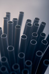 Bunch of black plastic straws scattered in container over plain grey background. Copy space for text