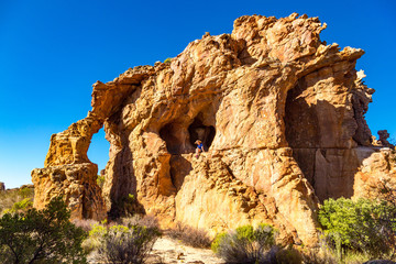 Spectacular rock formation with arch and cave, young woman sitting on an exposed rock, Stadsaal, Cederberg Wilderness Area, South Africa