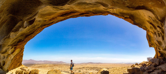 Panoramic view from a cave at Blutkuppe over the desert of Namib Naukluft Park, a man walking under the rock dome, Namibia, Africa
