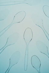 Scattered plastic spoons over blue background. Collecting plastic waste to recycling. Concept of plastic pollution and too many plastic waste. Copy space at the top