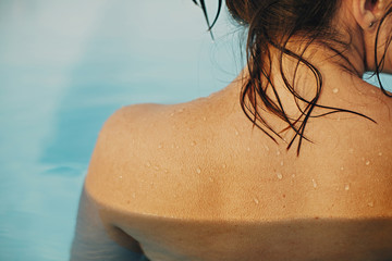 Beautiful woman shoulder with water drops close up, relaxing in pool. Back view of brunette girl...