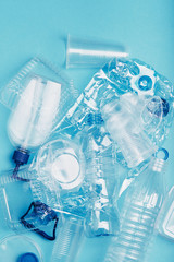 Squashed empty plastic bottles, cups, packagings, market bags and caps over blue background. Collecting plastic waste to recycling. Concept of plastic pollution and too many plastic waste
