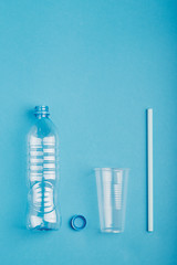 Empty plastic bottle, cup, straw and cap over blue background. Collecting plastic waste to recycling. Concept of plastic pollution and too many plastic waste. Copy space at the top