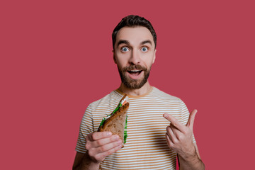 Bearded handsome charismatic man points his finger at a sandwich with surprise and a shocked...