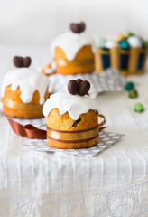 Easter cakes with sugar glaze or icing, chocolate eggs and brown ribbon on white tablecloth