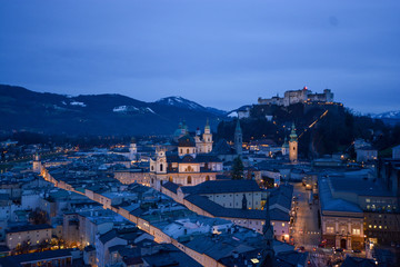 Salzburg evening cityscape with main Cathedral, Kollegienkirche and illuminated streets of old town on background of mountains in clouds