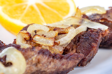 Roast beef with onion and lemon on a white plate.
