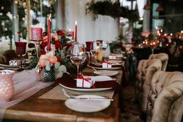 Romantic red table, decorated table with flowers and red candles. Luxury Christmas evening or wedding party decoration.