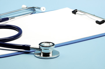 Close up on stethoscope and writing pad paper clip board on light blue background with copy space,...