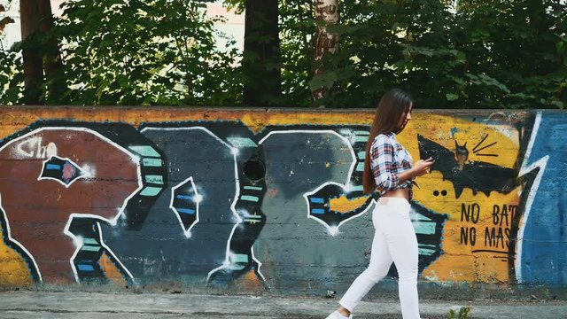 The girl is walking along the graffiti wall background. Copy space. 4K.