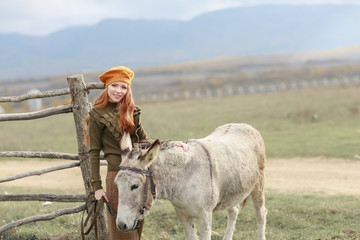 A woman on an animal farm near a wooden wicker fence walks a donkey.