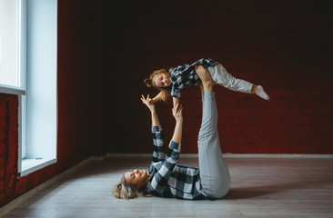 Young sporty mother and little girl doing stretching gymnastic exercises together  in loft studio