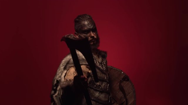 The Viking stands in a fighting position, pointing the battle axe towards the camera. A robber in armor and war paint looks madly at the camera holding an axe at the ready