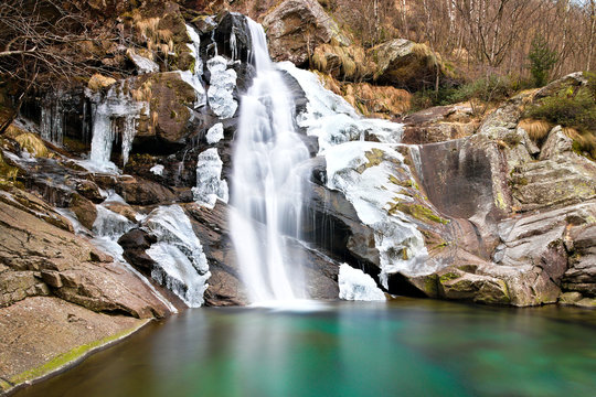 Beautiful winter waterfall surrounded by ice, shot with long exposure and silk water effect, in the Chiusella Valley, Piedmont, Italy