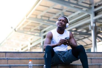 Happy good healthy and wellness concept. sport people and lifestyle concept. African american man sweating taking a break listening to music on phone after workout sitting on Stair at the city morning
