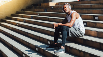  fitness, sport, workout people and lifestyle concept. African american man sweating taking a break listening to music on phone after workout sitting on Stair at the city morning
