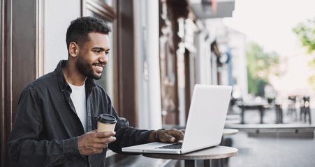 People city lifestyle young man sitting in a cafe using his laptop computer typing keyboard online outside banner panorama. Modern lifestyle, connection, business, freelance work concept