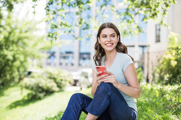 Young beautiful woman using smart phone in a city park.  Smiling girl resting outdoor. Student lifestyle, connection, business, freelance work, education concept