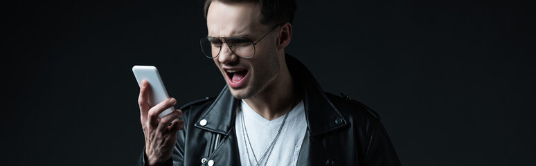 angry stylish man yelling at on smartphone isolated on black, panoramic shot
