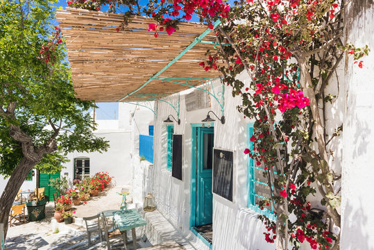 Fototapeta Traditional street with cute cafe bars in Greece. Beautiful colorful greek houses with flowers on Amorgos island