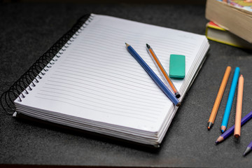 caderno com lápis caneta e borracha de apagar sobre uma superfície preta com alguns livro ao...