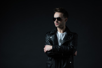 Fototapeta premium stylish brutal man posing in biker jacket and sunglasses isolated on black