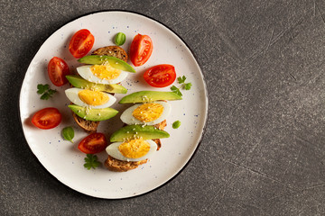 Avocado, egg on toast, tomatoes on  plate. Top view on a dark background.