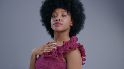 Amazing elegant black lady preparing for romantic date fixing her outfit and hair. Portrait of gorgeous african girl admiring herself in a mirror on grey background.